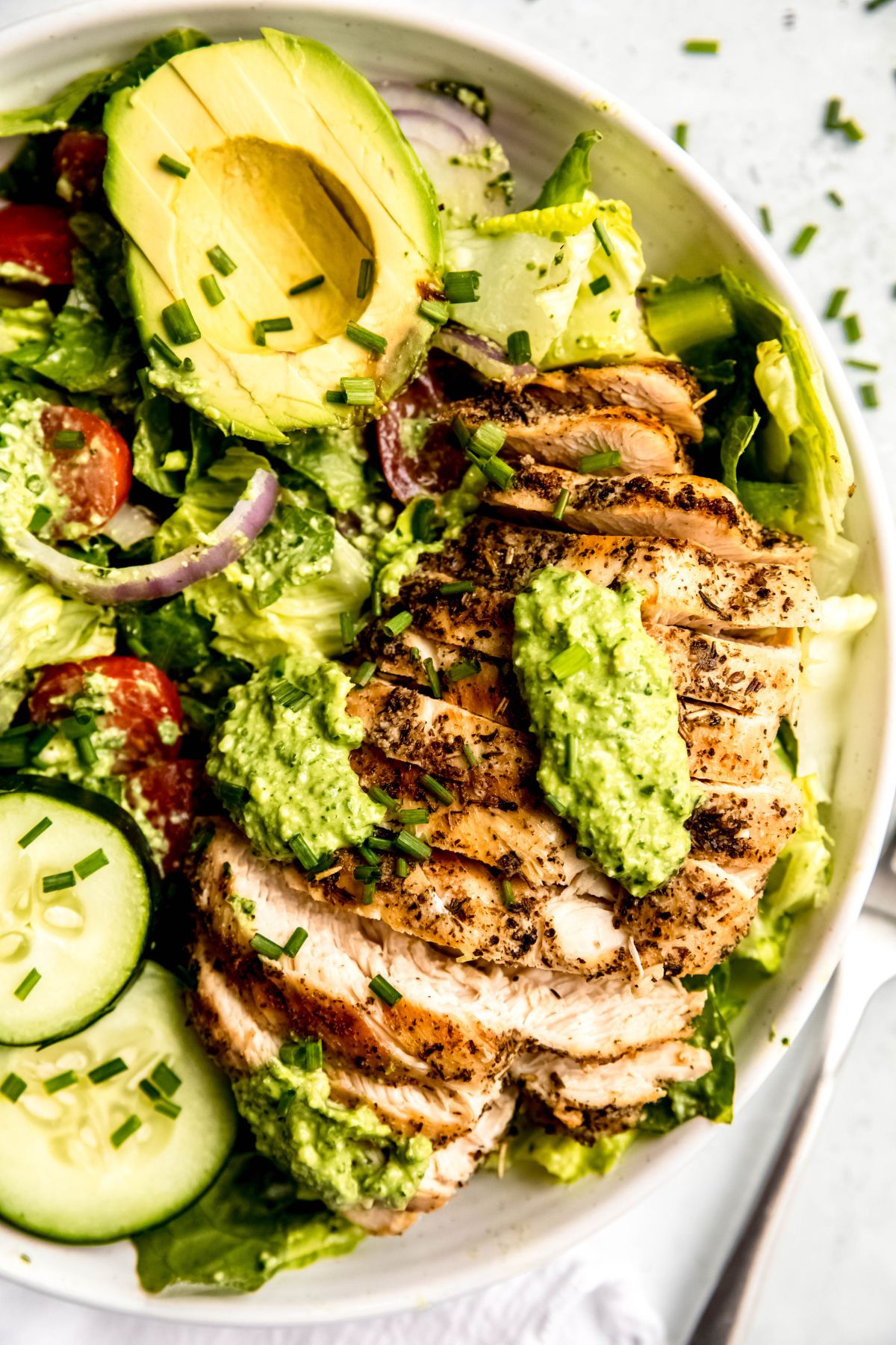 Grilled chicken green goddess salad in a large white bowl with cucumber and avocado.
