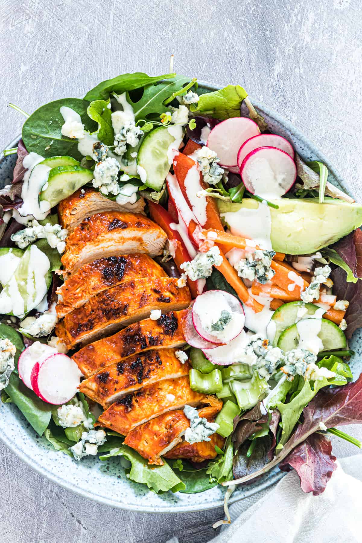 Buffalo chicken in a bed of lettuce with ranch dressing, radishes, and avocado.