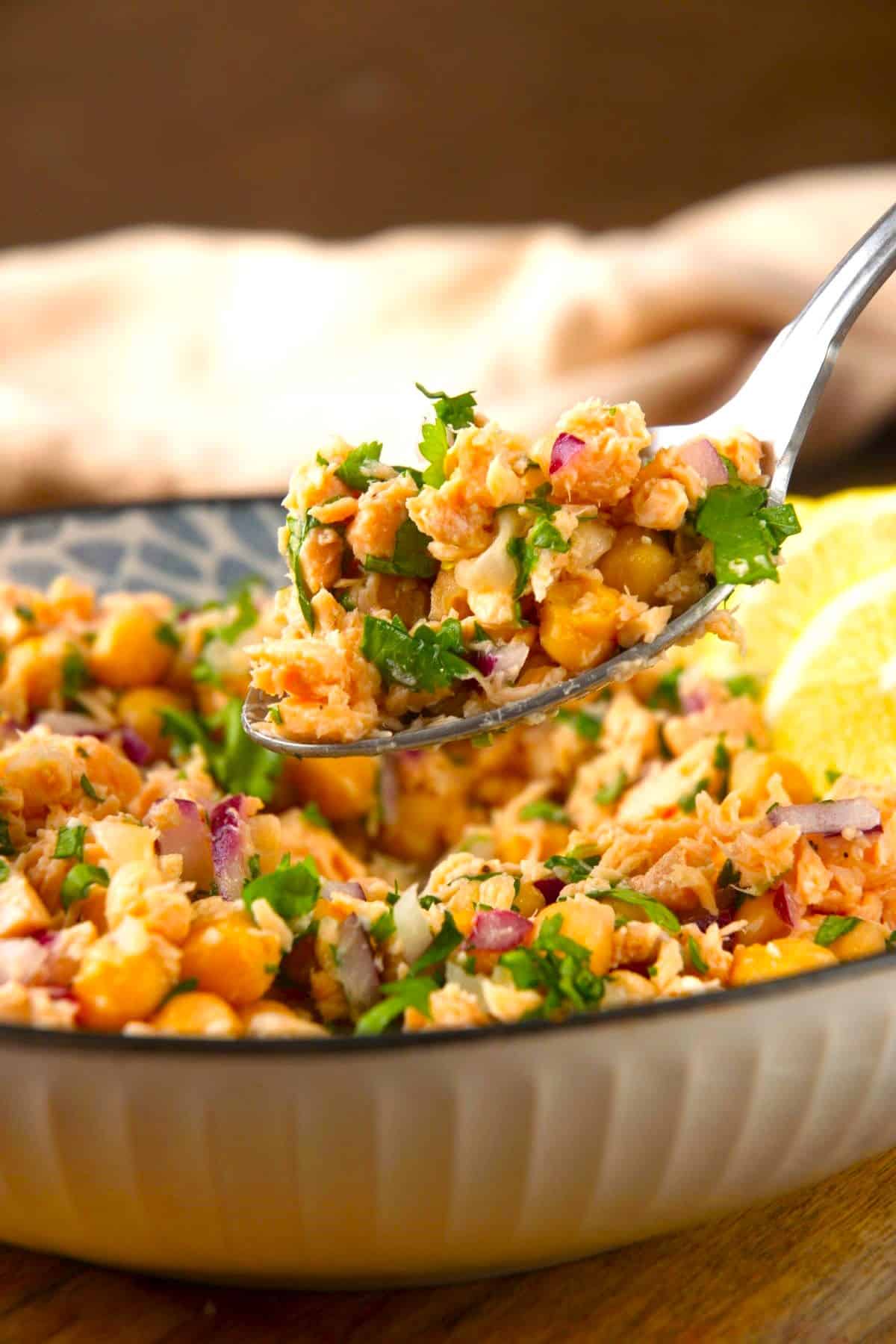 Chickpea salmon salad lifted from a bowl on a spoon with cilantro garnish.