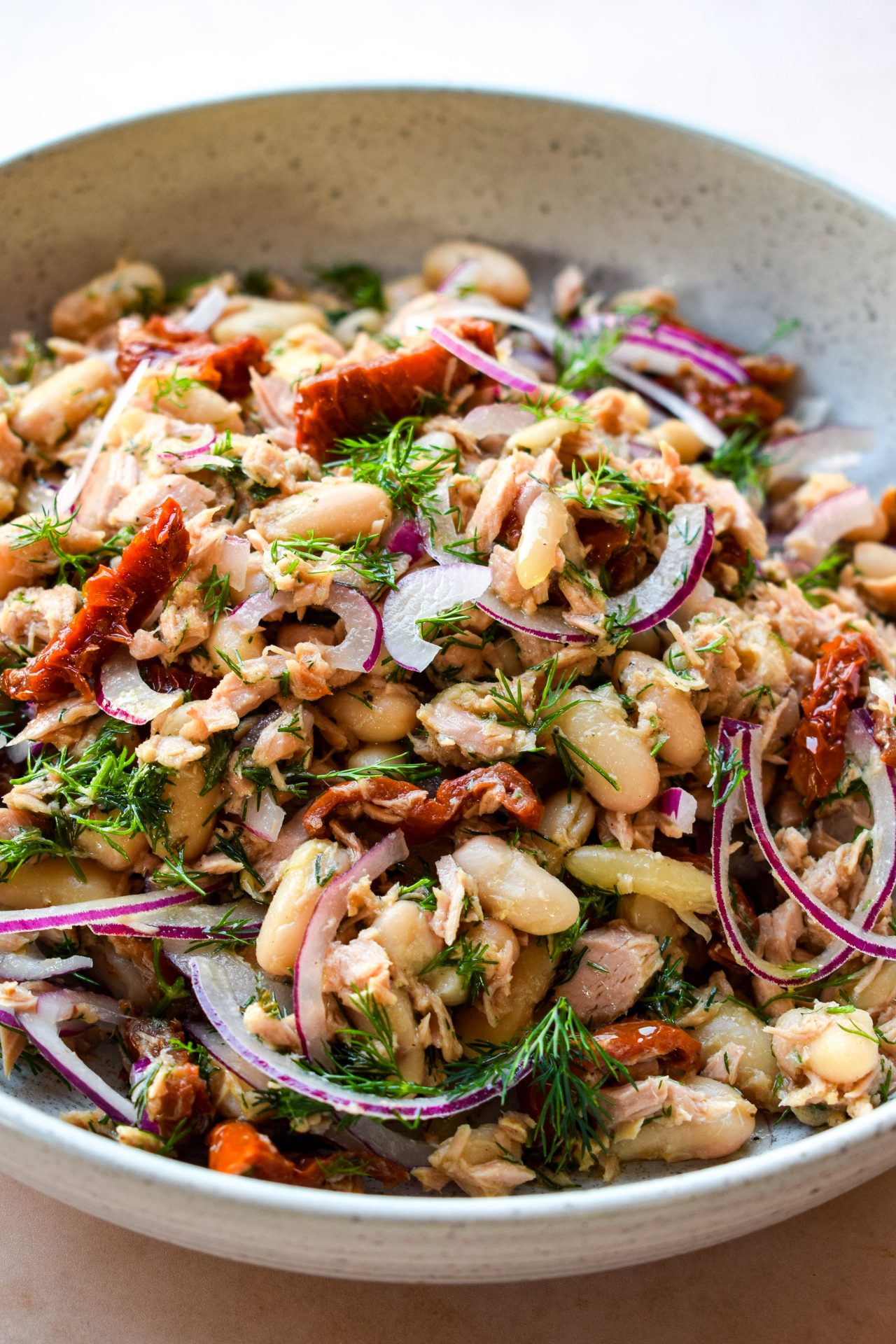 White bean tuna salad with sun-dried tomatoes with red onion in a white bowl.