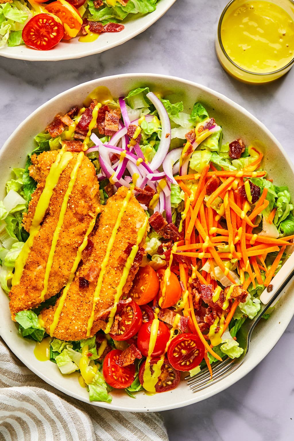 A green salad with red onion, carrots, tomatoes, chicken strips and honey mustard dressing.