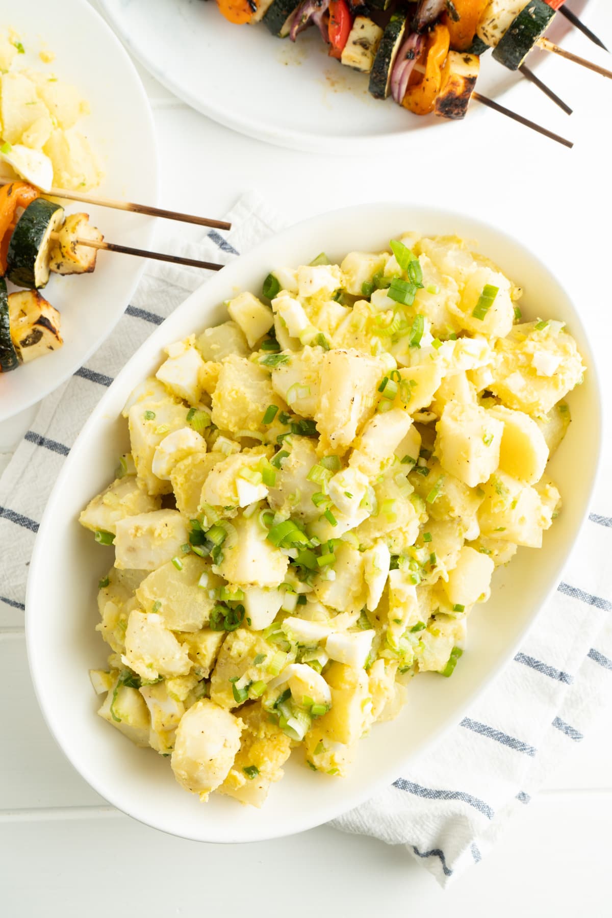 German potato salad without mayo and with green onion garnish in an oval white dish.