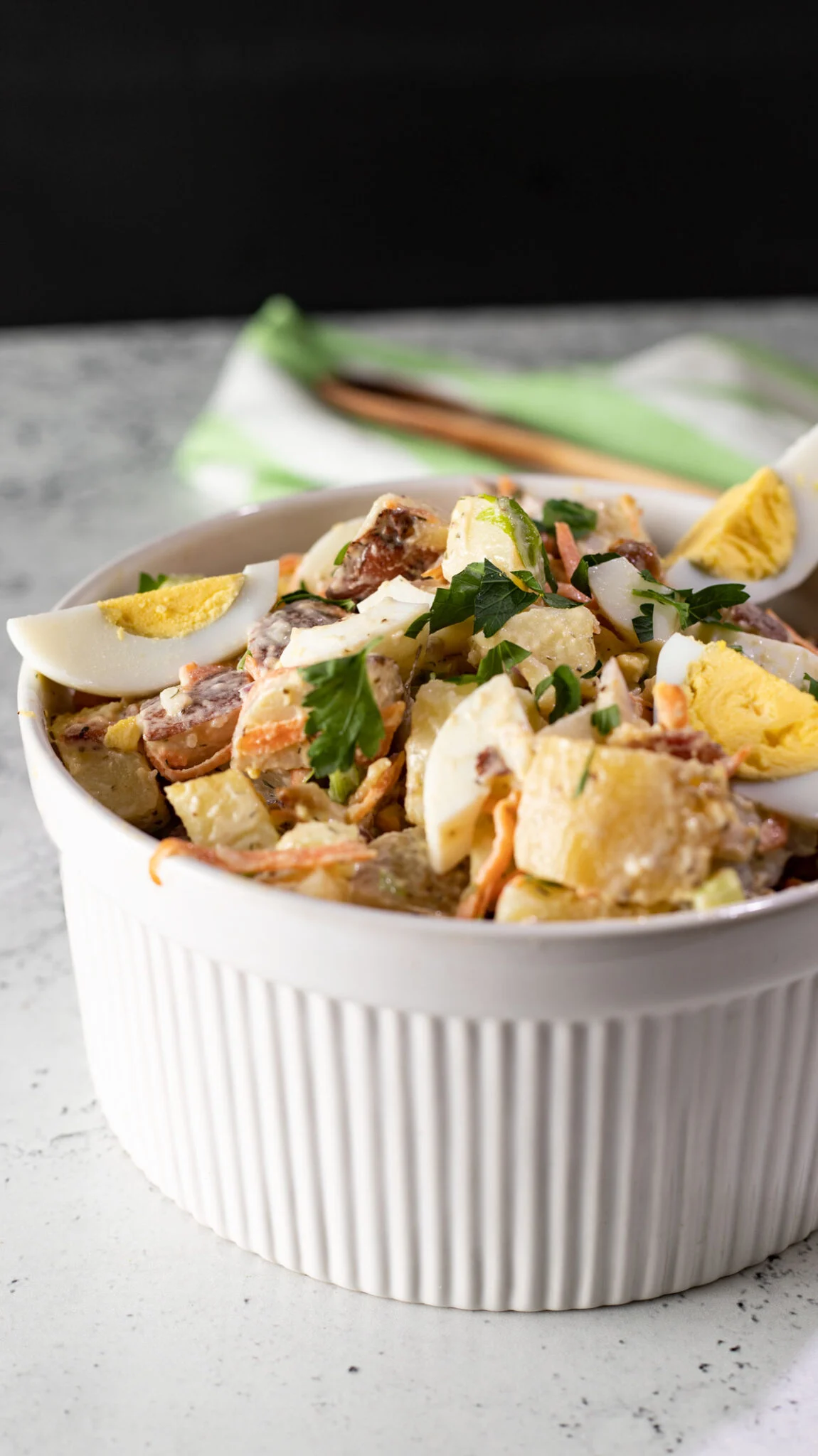 A side dish with boiled potatoes, bacon, and eggs, in a white ridged bowl.