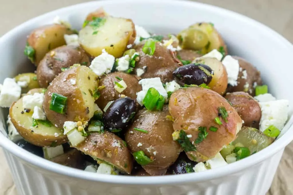 Boiled potatoes with feta and tangy dressing in a white ridged bowl.