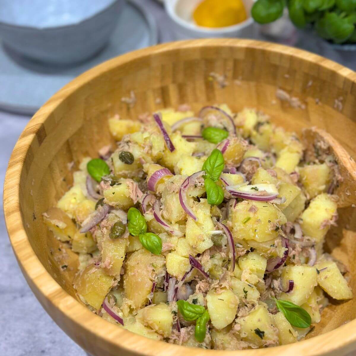 Tuna salad with potatoes and green garnish in a large wood bowl.