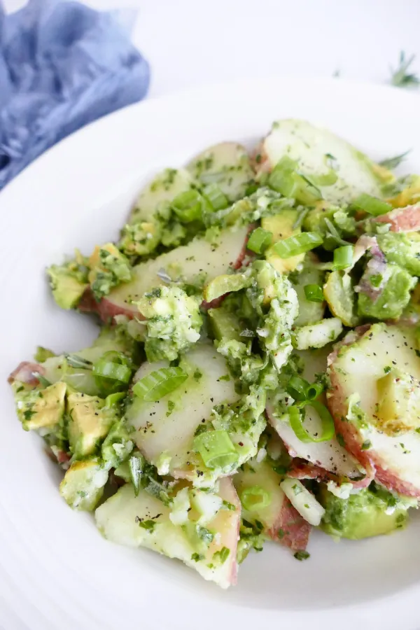 Herby red potato salad with green herbs on a white plate.