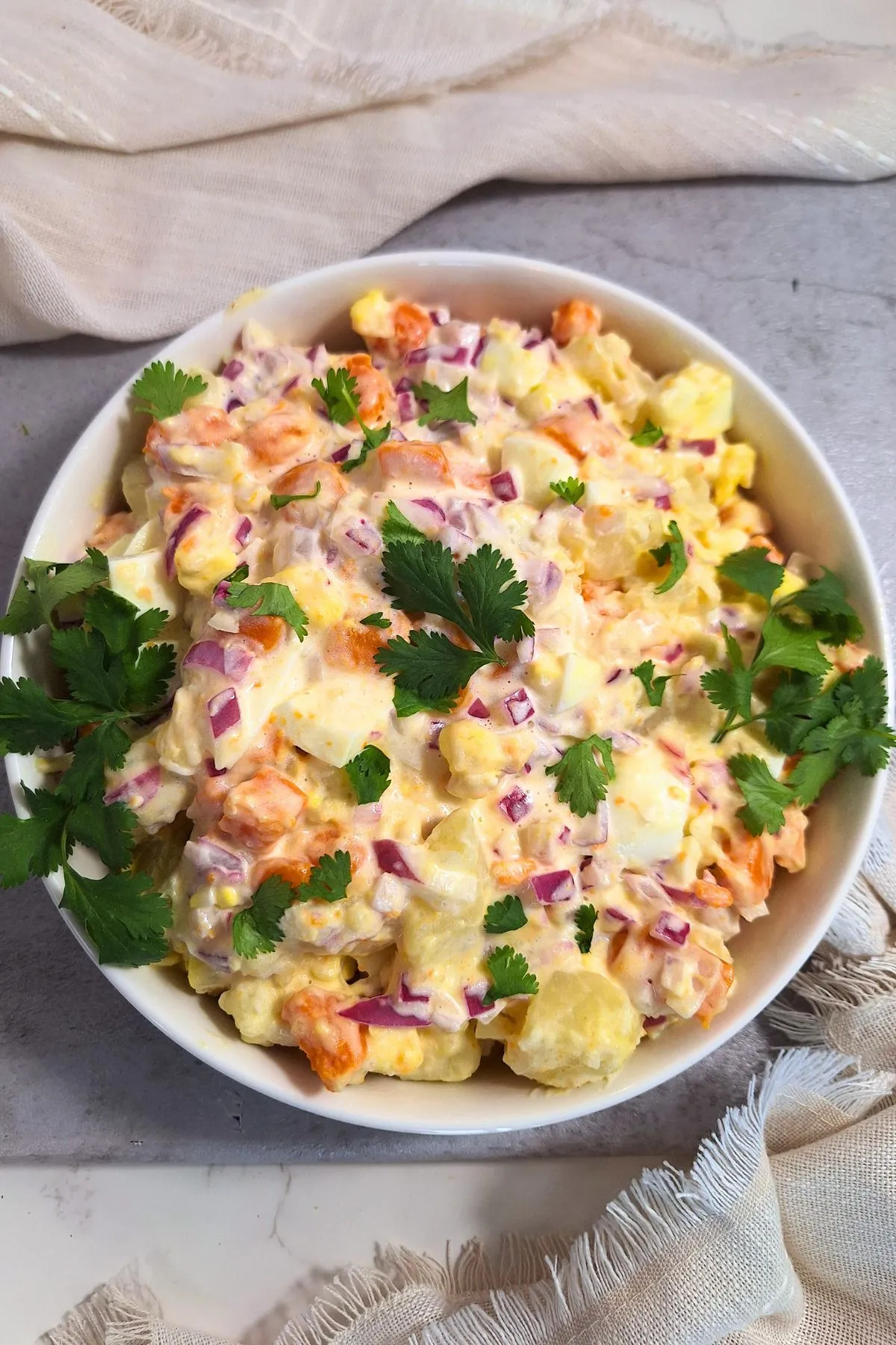 Dominican potato salad with red onion and carrots in a white bowl with green garnish.
