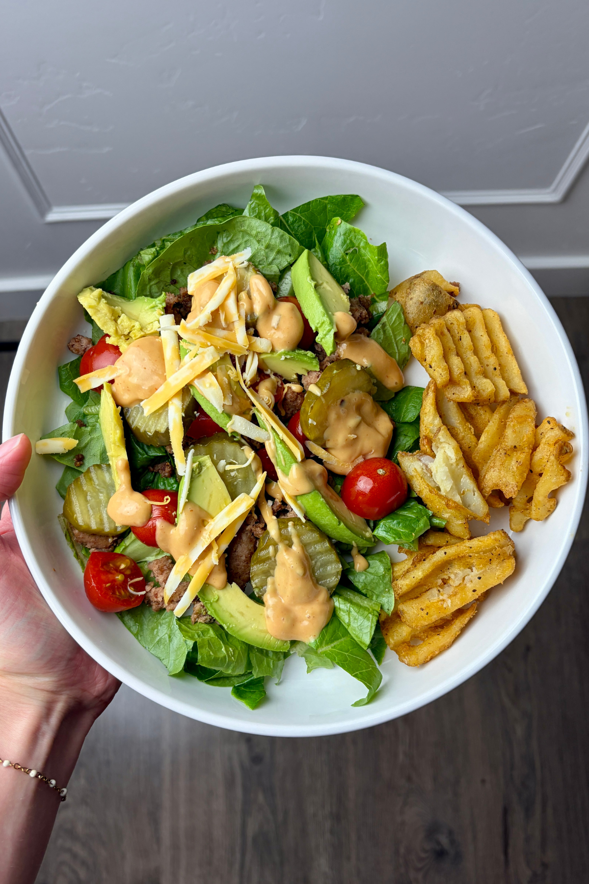 Woman holding white bowl with ingredients for high protein burger bowl.