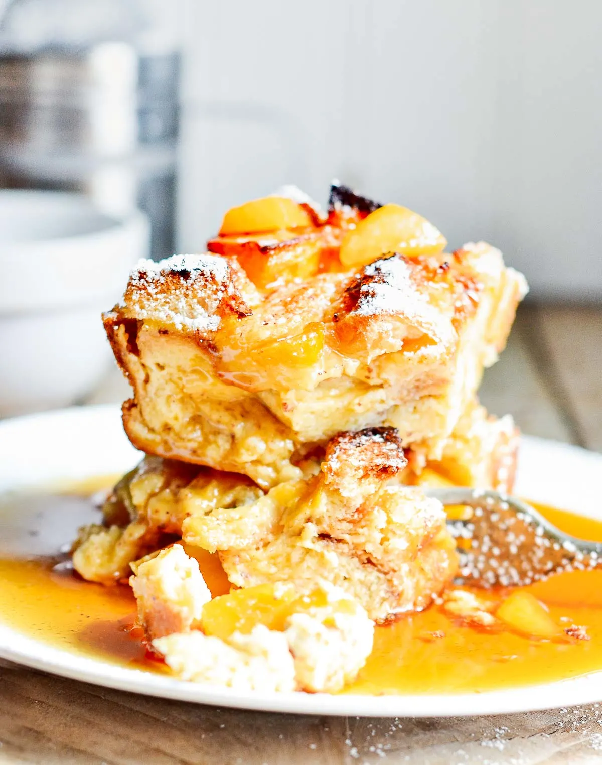 Slices of peach French toast casserole on a white plate in a puddle of syrup.
