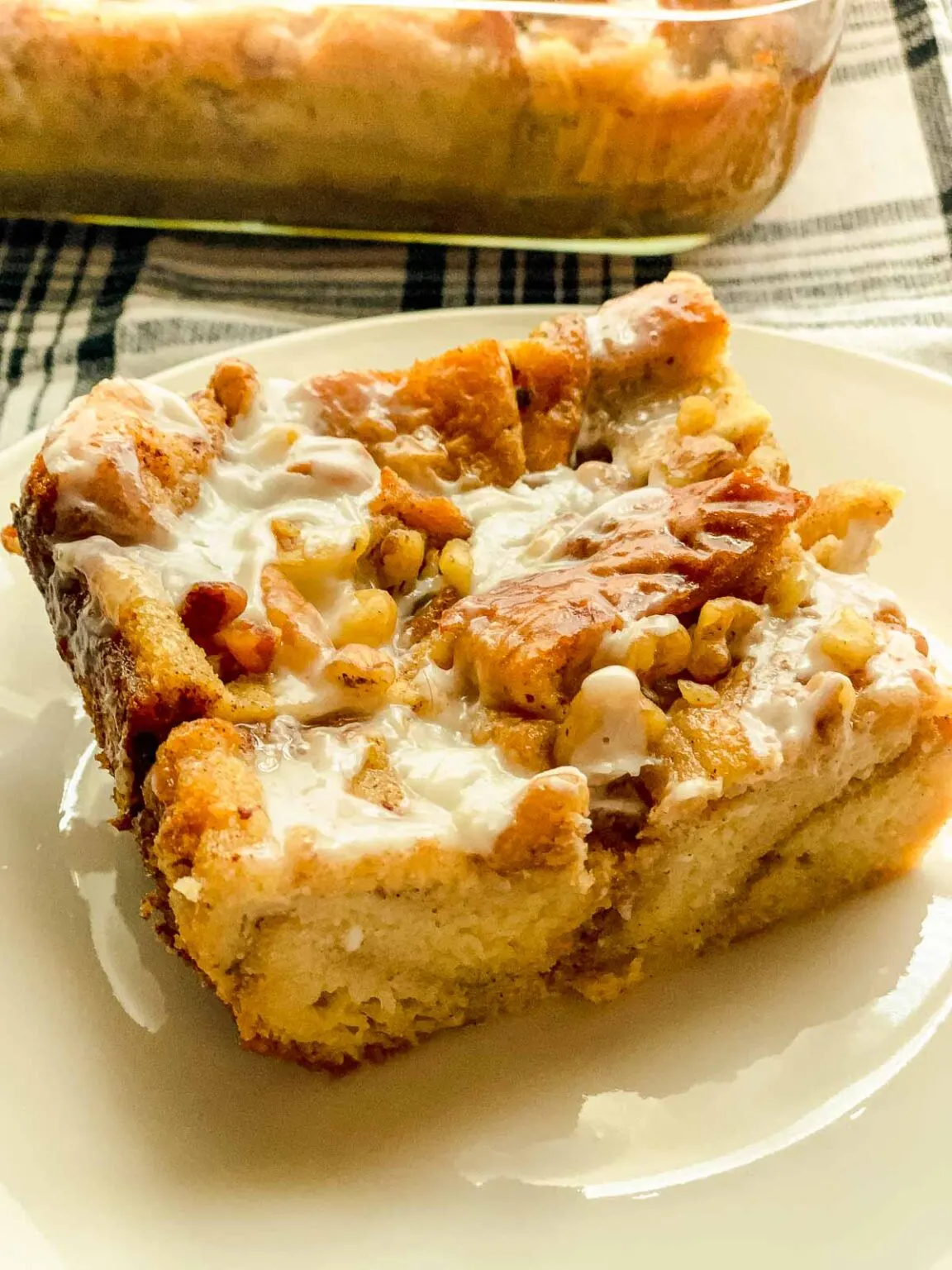 A square slice of French toast bread pudding on a cream plate in front of the glass casserole dish.