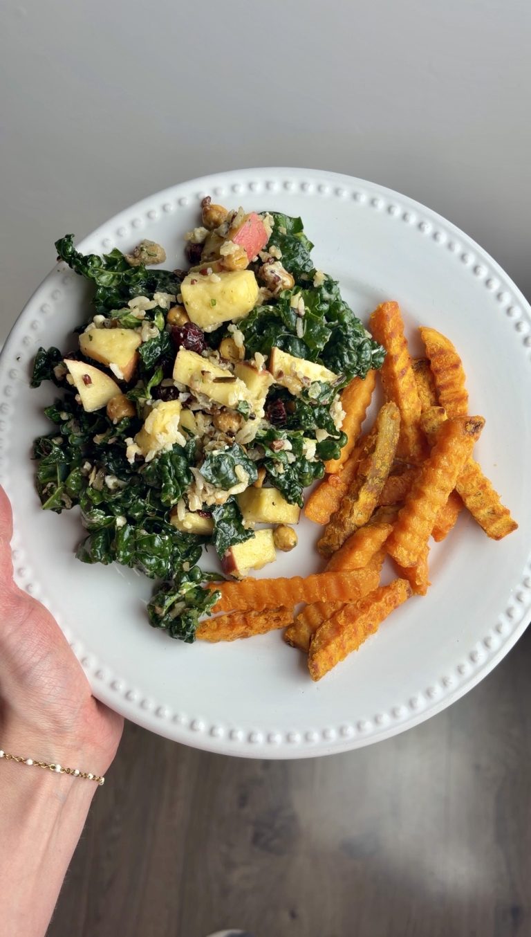 Woman holds white plate with chickpea kale salad and sweet potato fries.