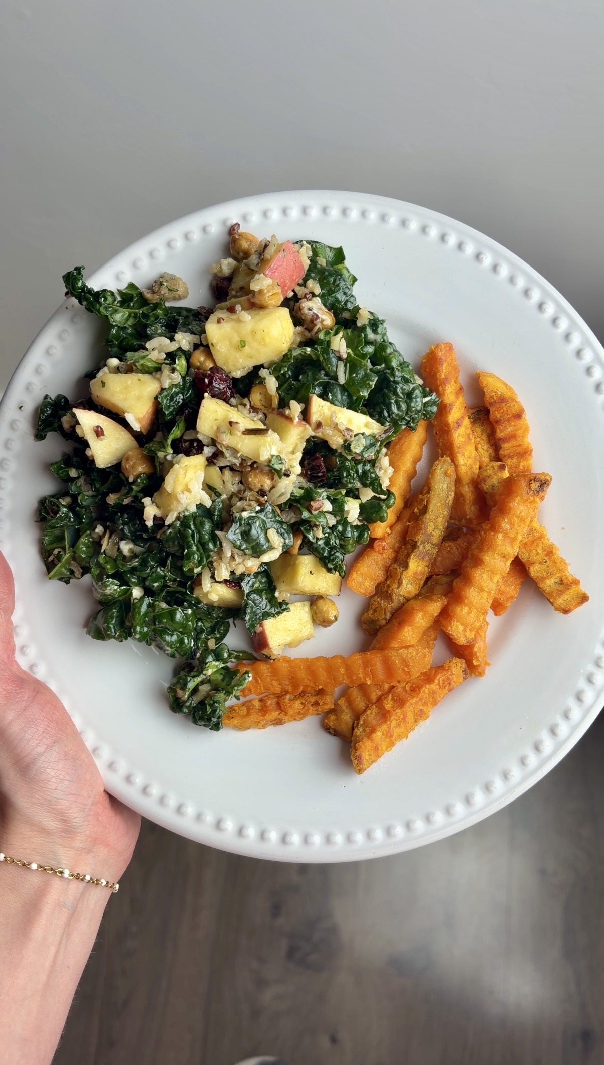Woman holds white plate with chickpea kale salad and sweet potato fries.