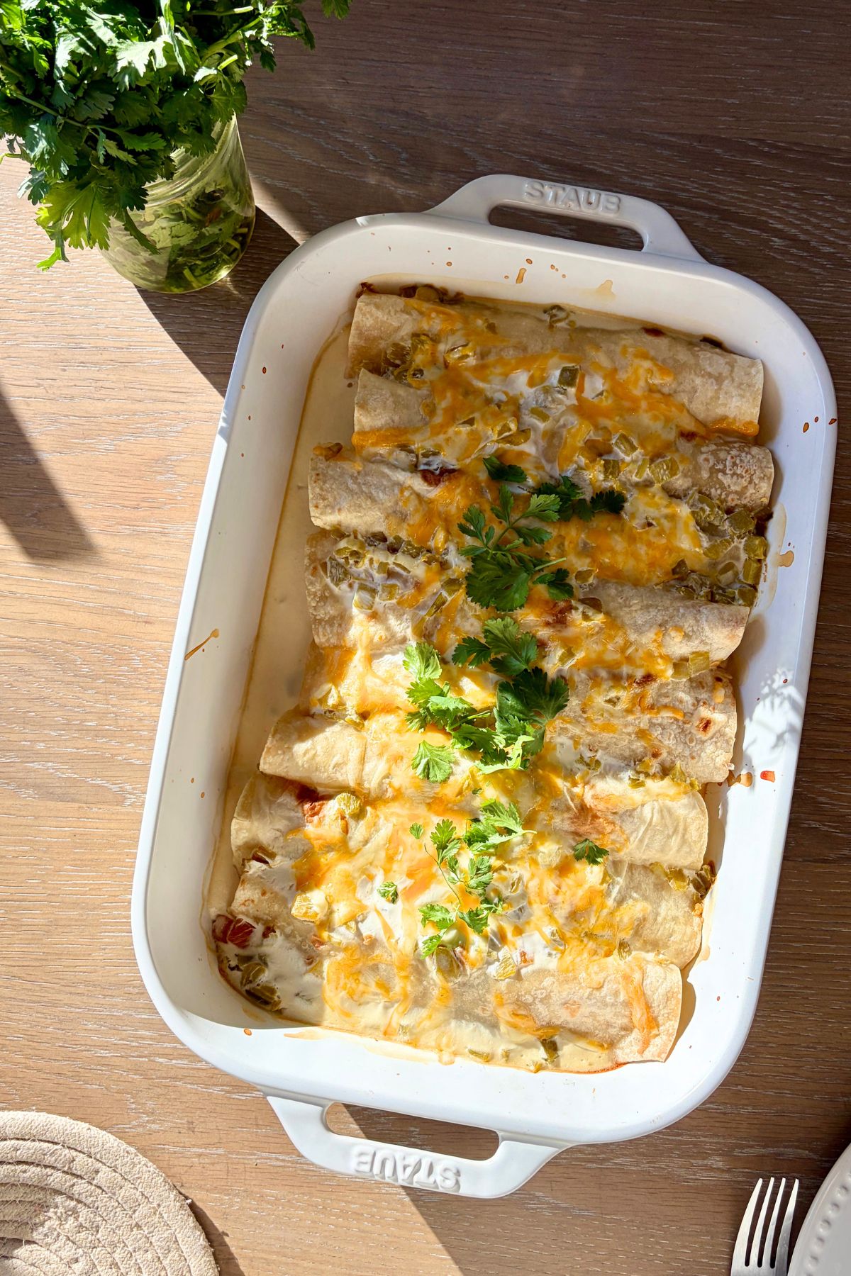 A white casserole dish filled with cheesy chicken enchiladas with cilantro garnish on top.