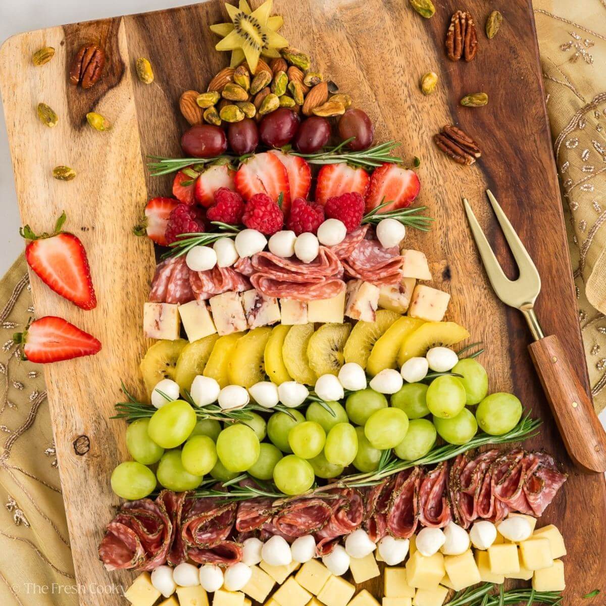 A Christmas tree-shaped charcuterie spread with meat, cheese, fruit, and nuts.