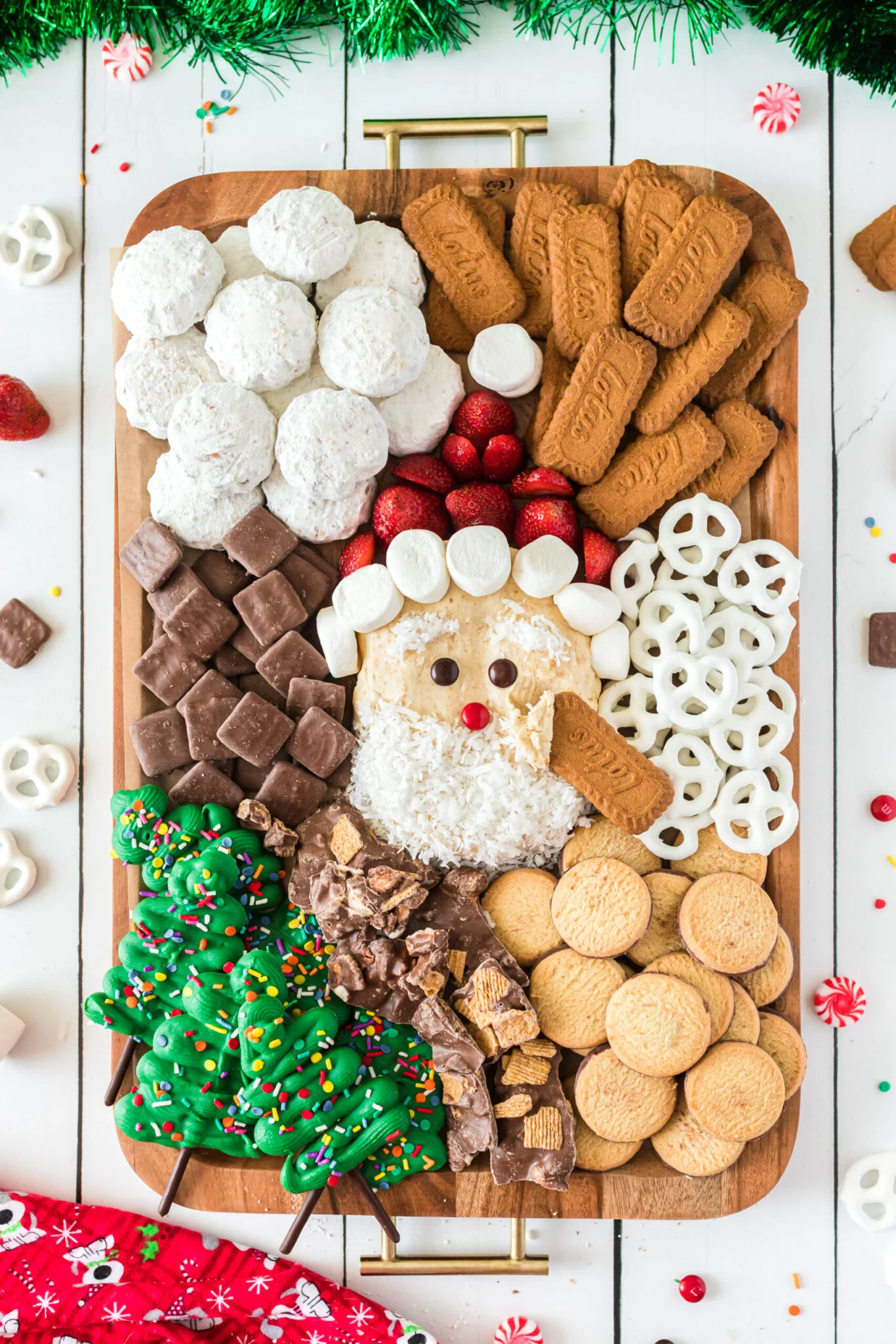 A Christmas dessert charcuterie board with a cheesecake dip Santa, cookies, and treats.