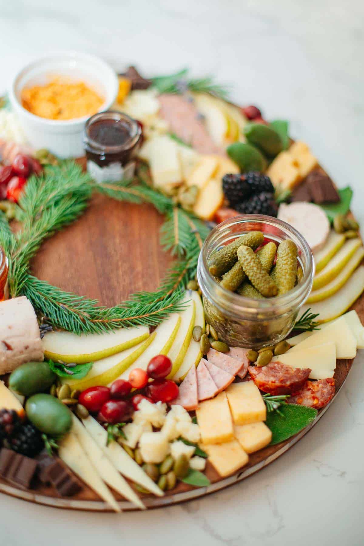 A Christmas wreath charcuterie board on a round wooden board with meat, cheese, fruit, and veggies.