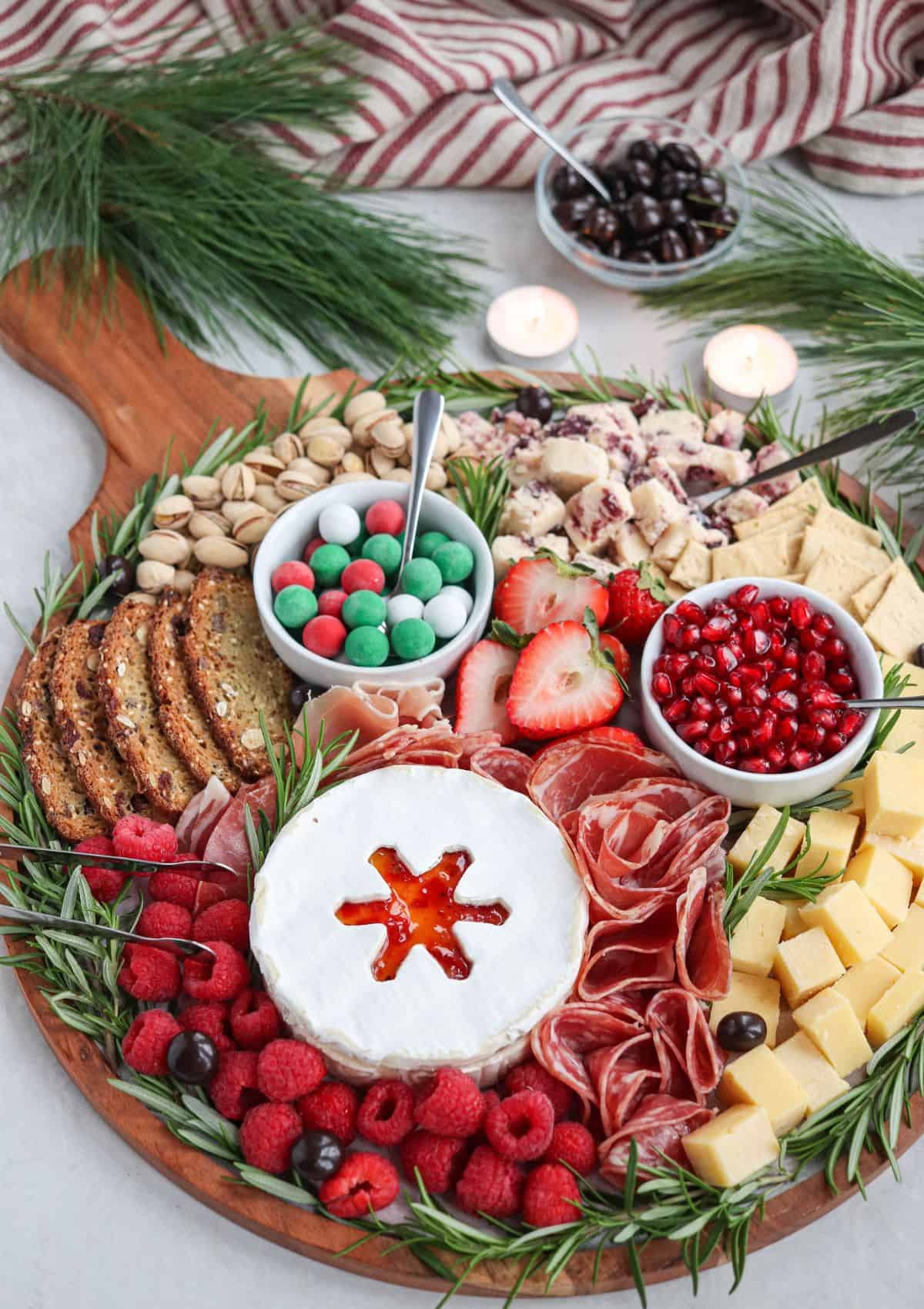 A Christmas charcuterie board with fruit, crackers, cheese, and sweets.