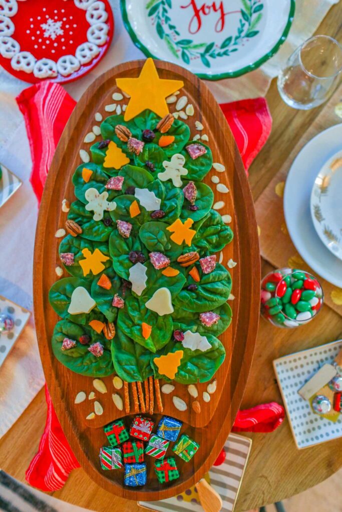 A spinach charcuterie salad shaped like a Christmas tree with cheese cutout ornaments and stars.