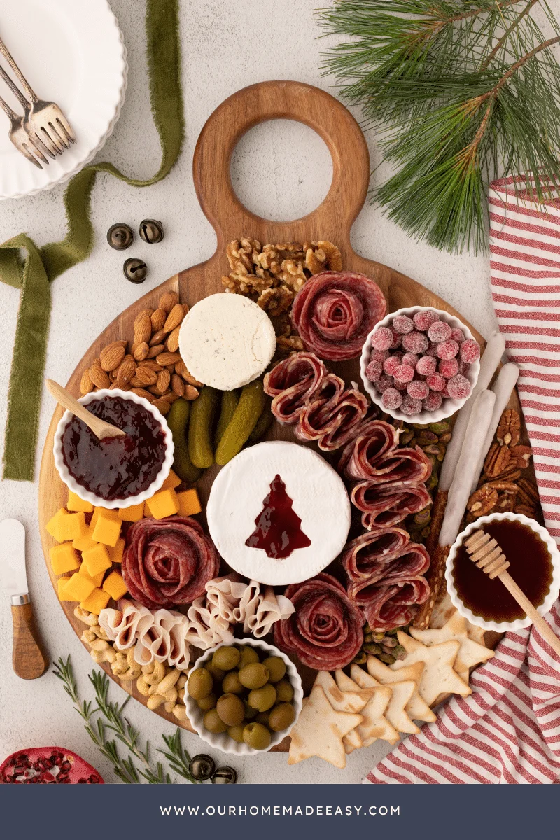 A Christmas-themed meat and cheese charcuterie board, featuring a wheel of brie with a Christmas tree cutout and pepper jelly underneath.