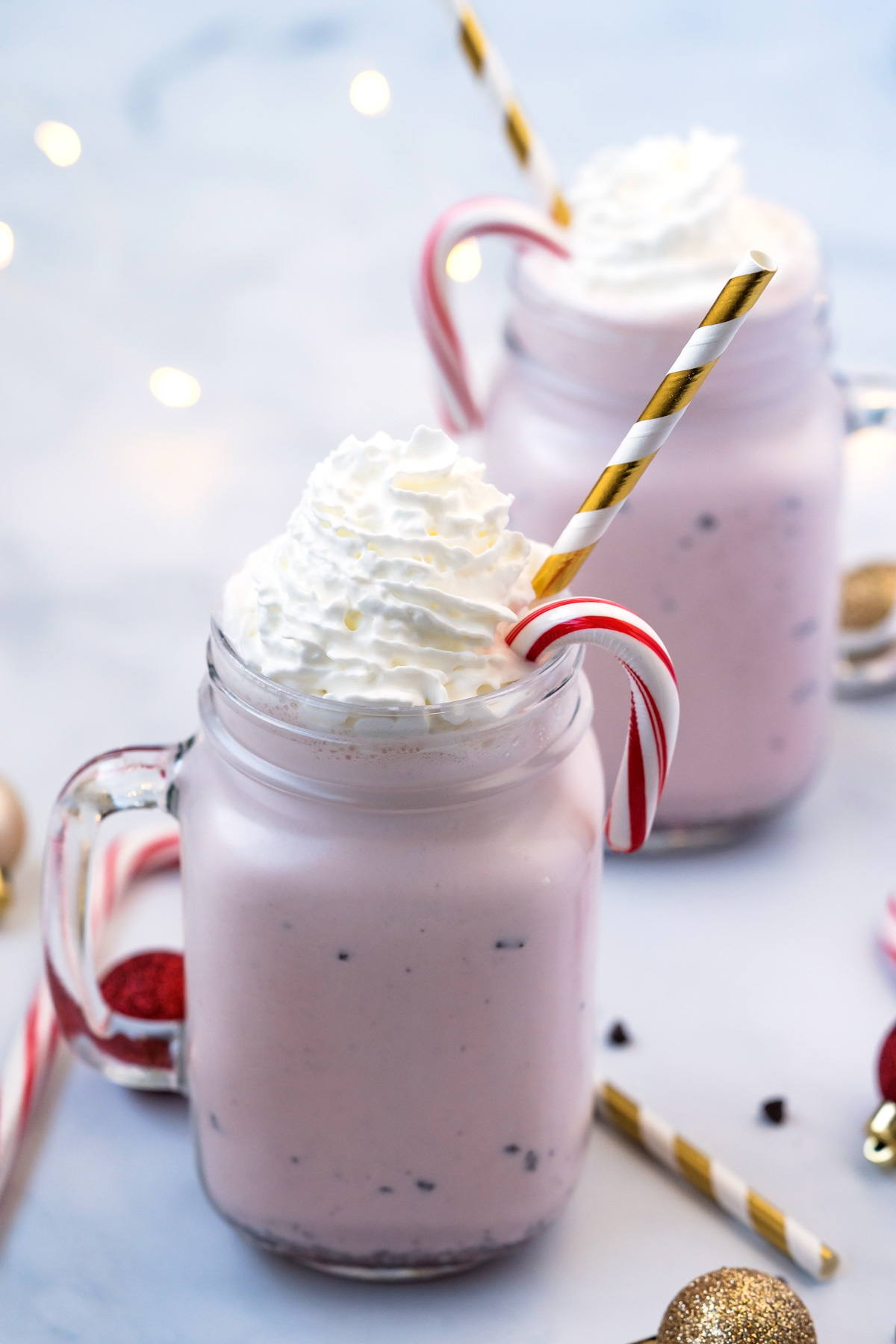 Peppermint milkshakes in two mason jars with whipped cream on top and striped gold and white straws.