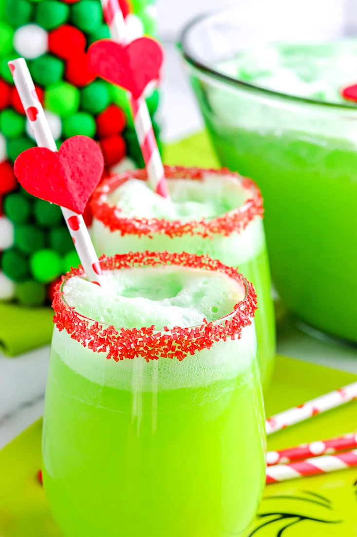 Grinch punch in a large bowl and in two glasses rimmed with red sprinkles.