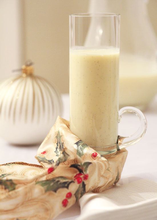 Christmas drinking custard in a large thin glass with a Christmas towel and ornament in the background.