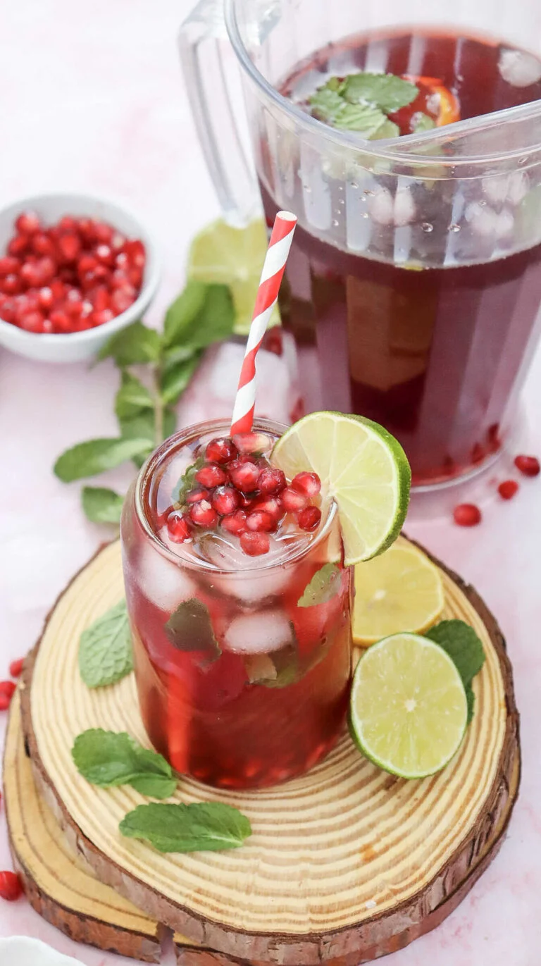 Pomegranate fizz mocktail in a glass and pitcher with lime, mint, and pomegranate garnish,