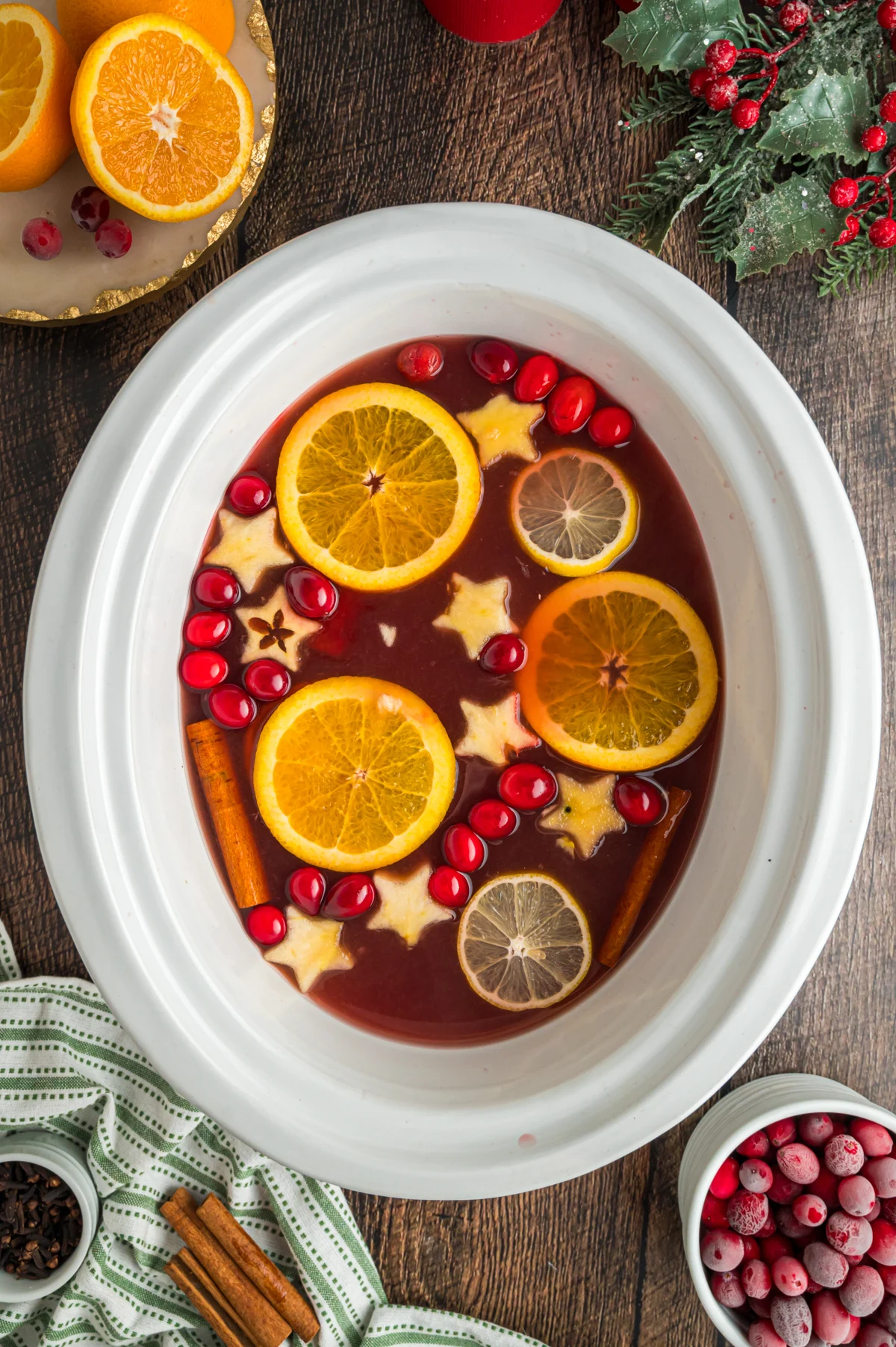 Christmas bunch in a white crockpot with sliced oranges and apples cut into the shape of stars.