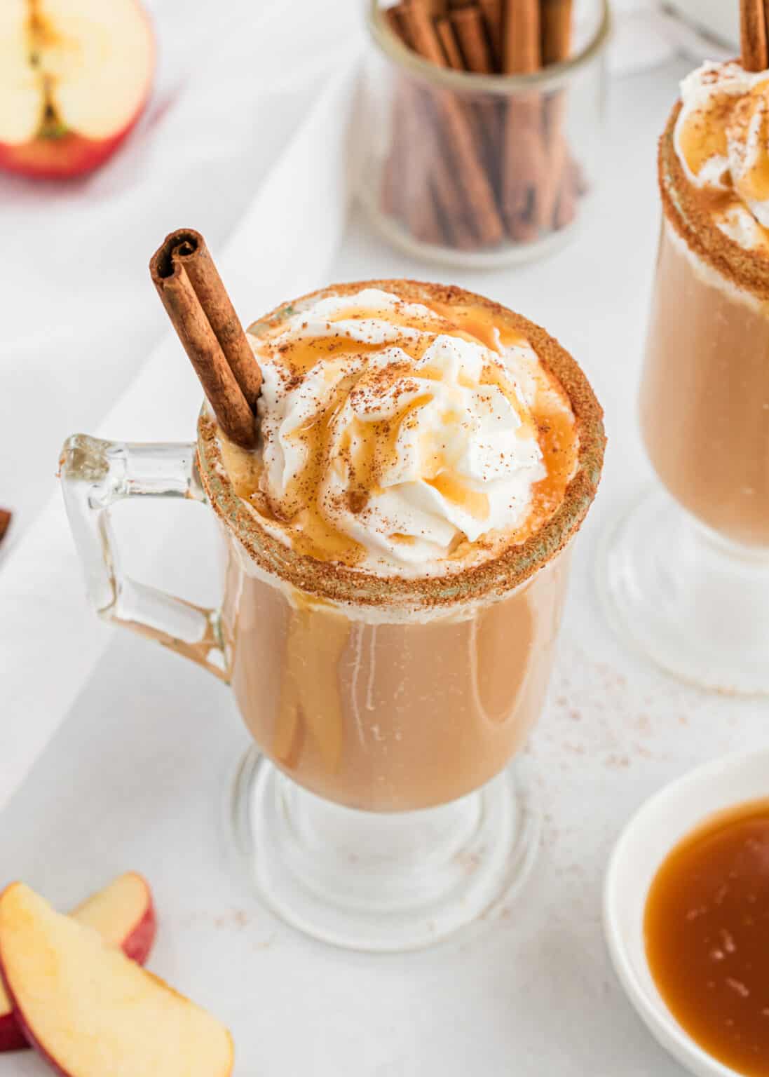 Caramel apple cider in tall glass mugs with whipped cream and cinnamon topping.