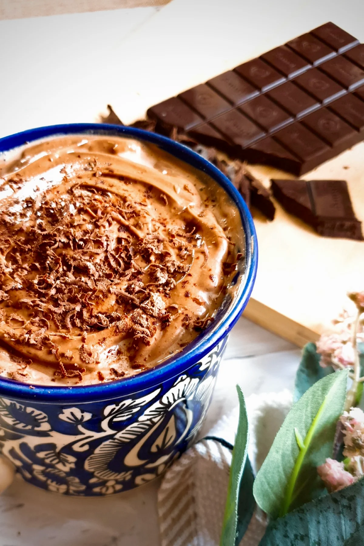 Whipped chocolate Christmas drink in a blue and white decorative mug next to a bar of chocolate.