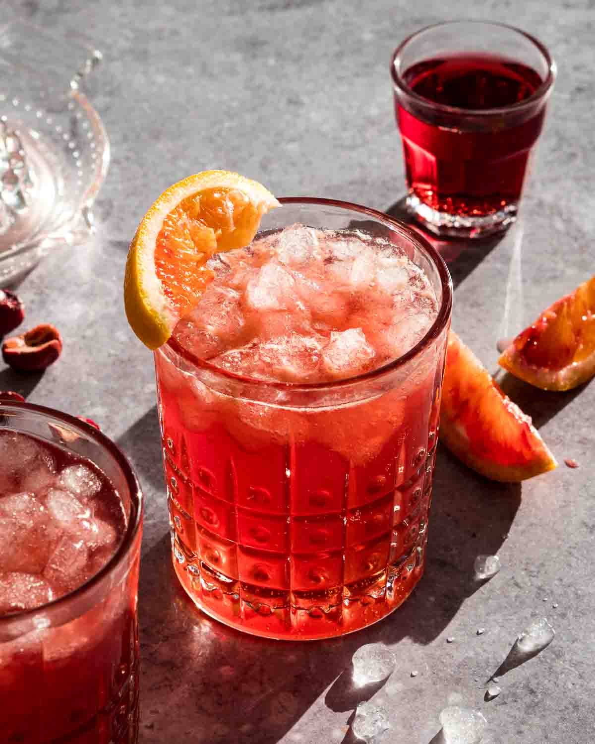 A cranberry mocktail in a glass with ice and an orange wedge for garnish.