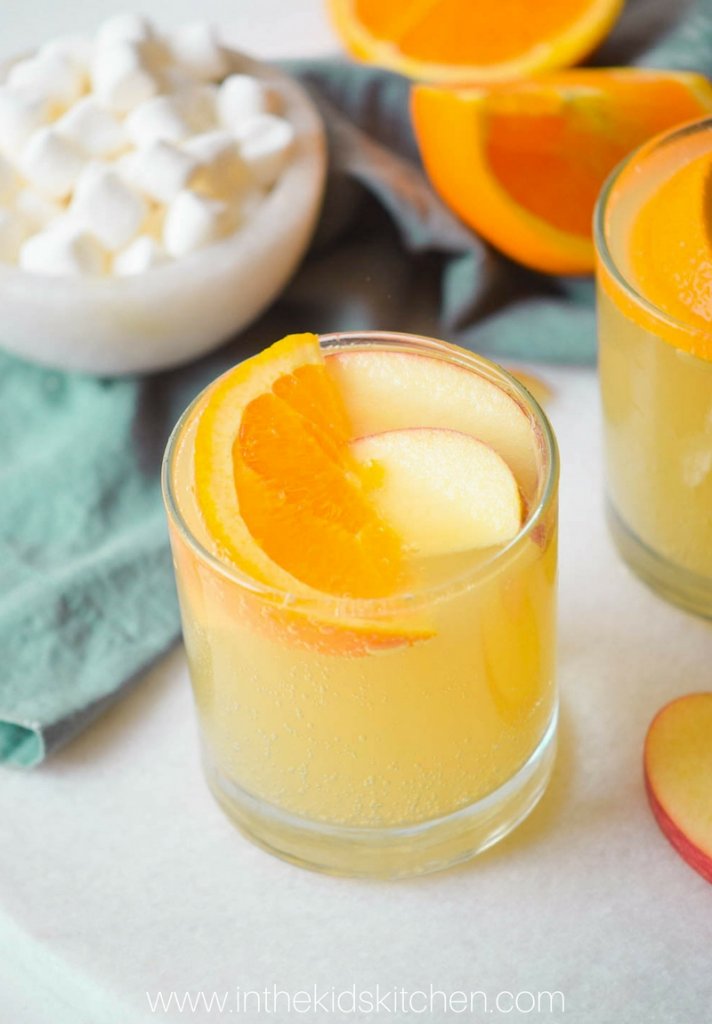 A fizzy orange Christmas drink into clear glasses with orange slices for garnish.