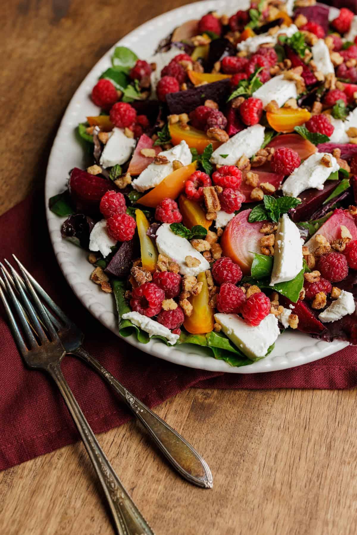 Beet and berry salad with greens and white cheese on a large white oval platter.