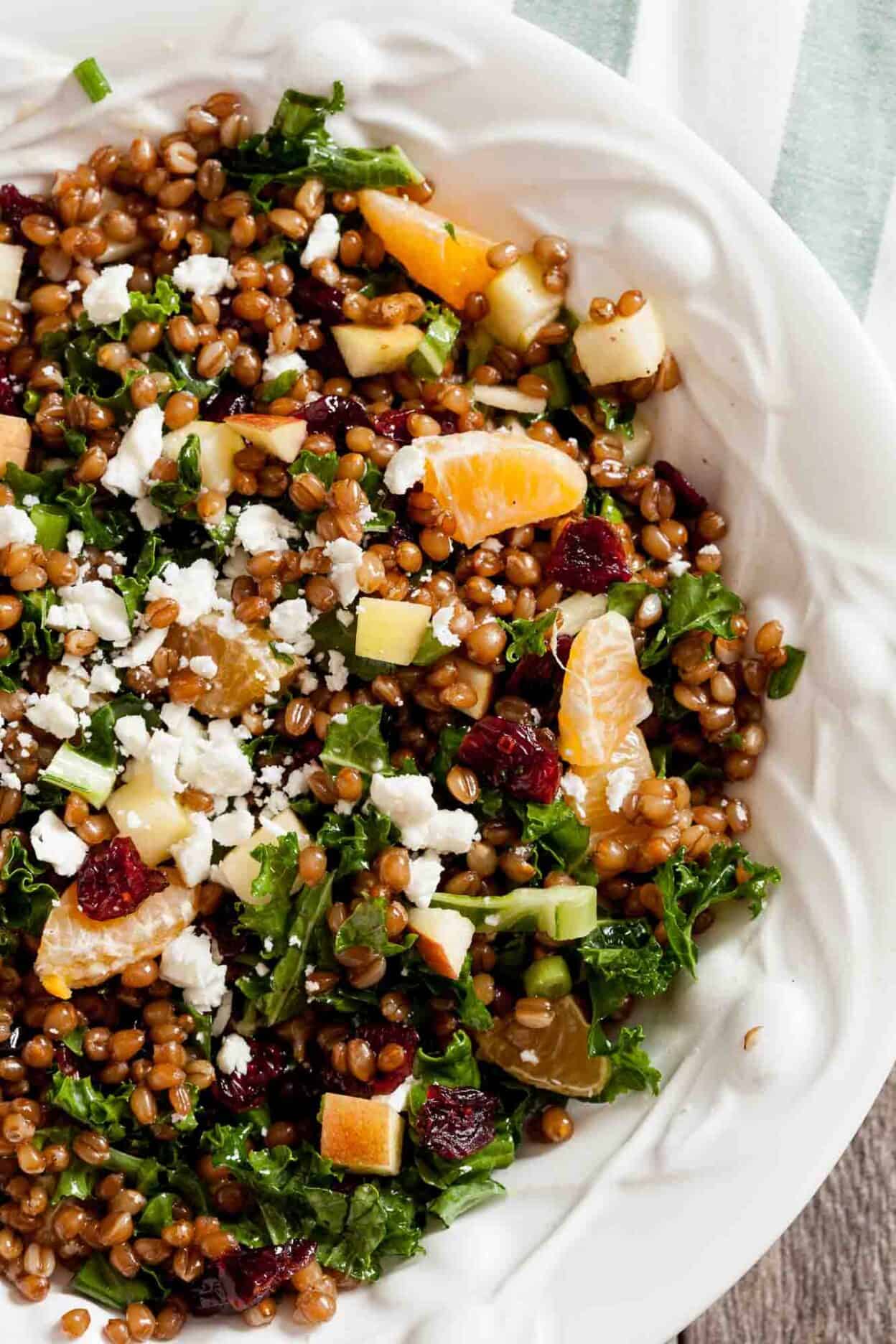 Wheat berry salad with greens, mandarin oranges, and cheese, in a decorative white serving bowl.