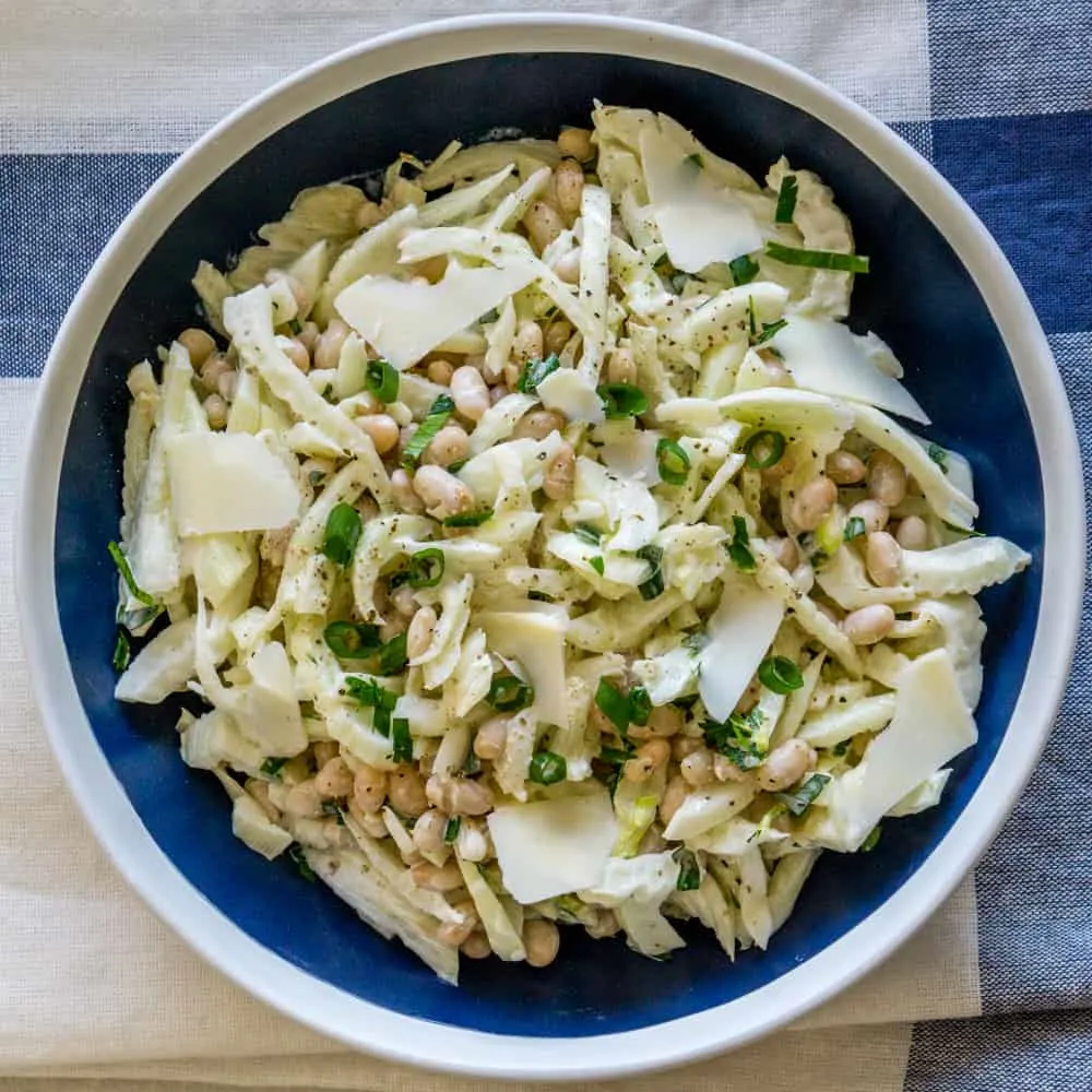 Shaved fennel salad with white beans and parmesan cheese in a blue and white bowl.