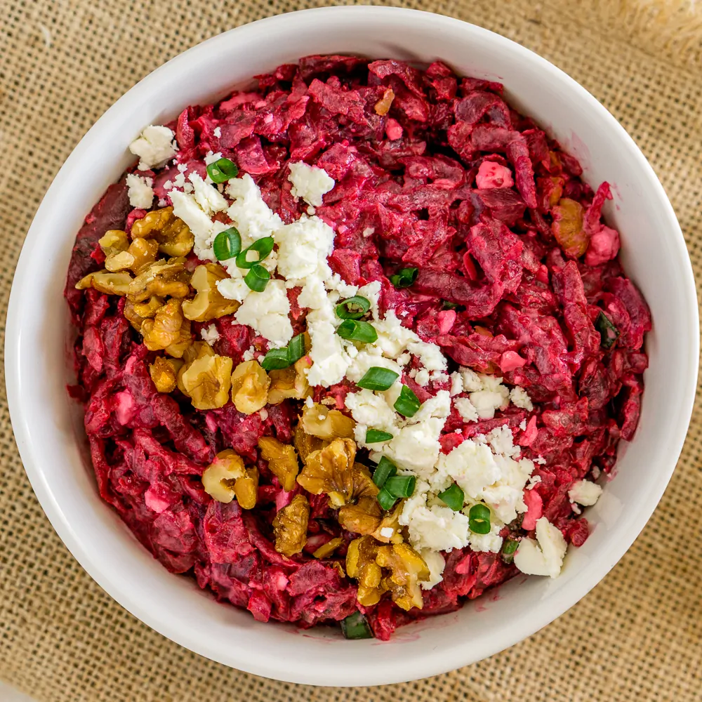 Russian beet salad with feta and walnuts in a white bowl.