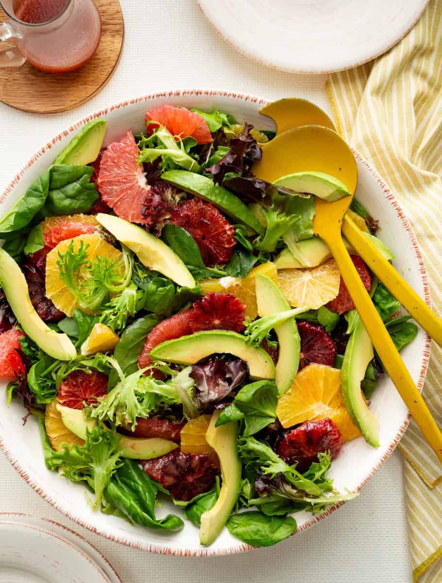 Citrus beet green salad in a white bowl with serving spoons.