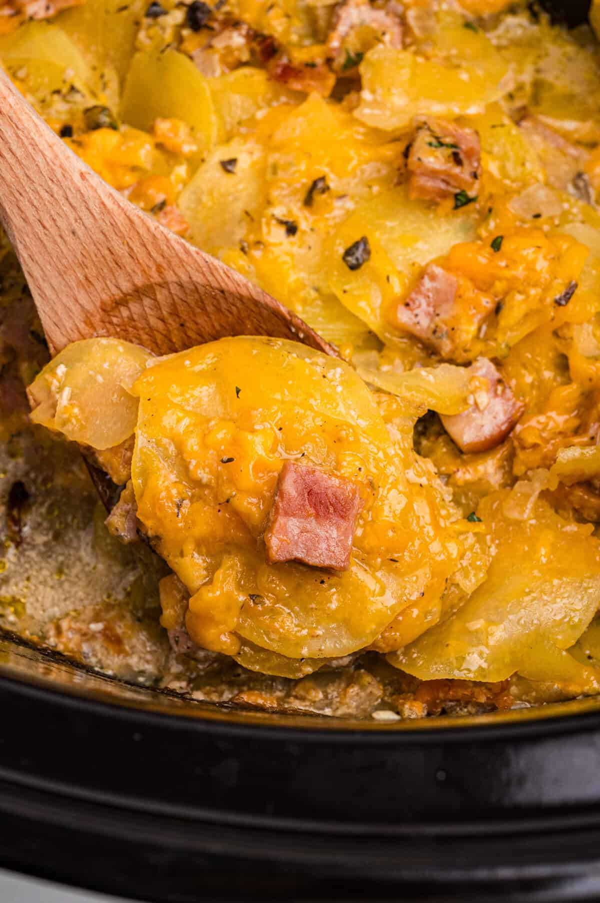 Cheesy scalloped potatoes with diced ham in a black crockpot.