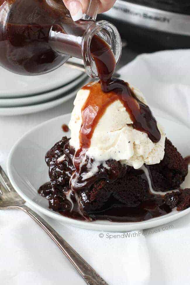 Chocolate lava brownies with ice cream on top and chocolate syrup being poured over the whole dessert.