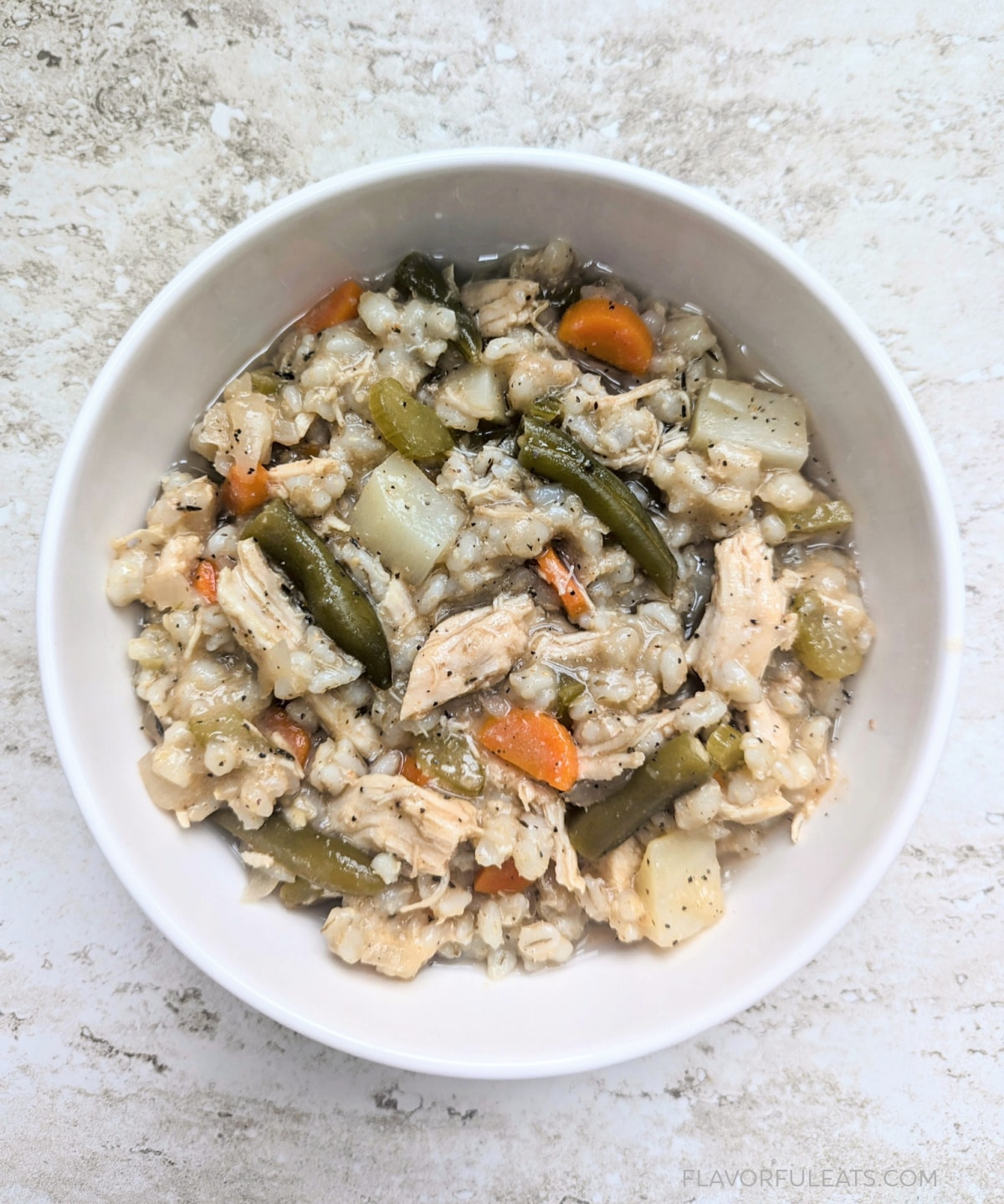 Chicken barley stew with carrots and green beans in a white bowl.