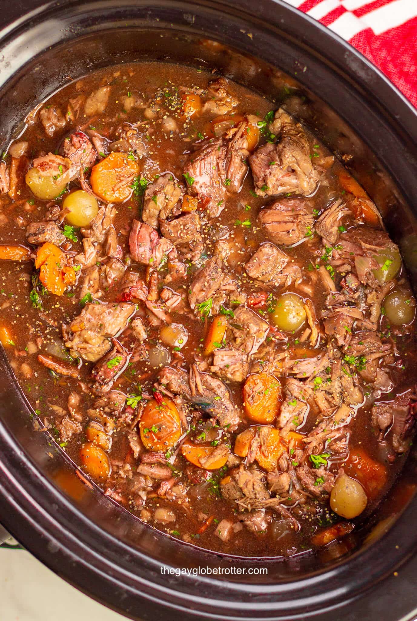 Beef stew with carrots and potatoes in a large black slow cooker.