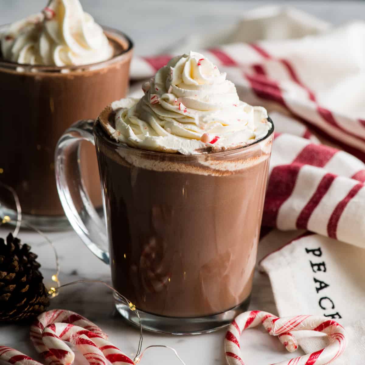 Two clear glass mugs with peppermint hot chocolate, whipped cream, and crushed peppermint on top.