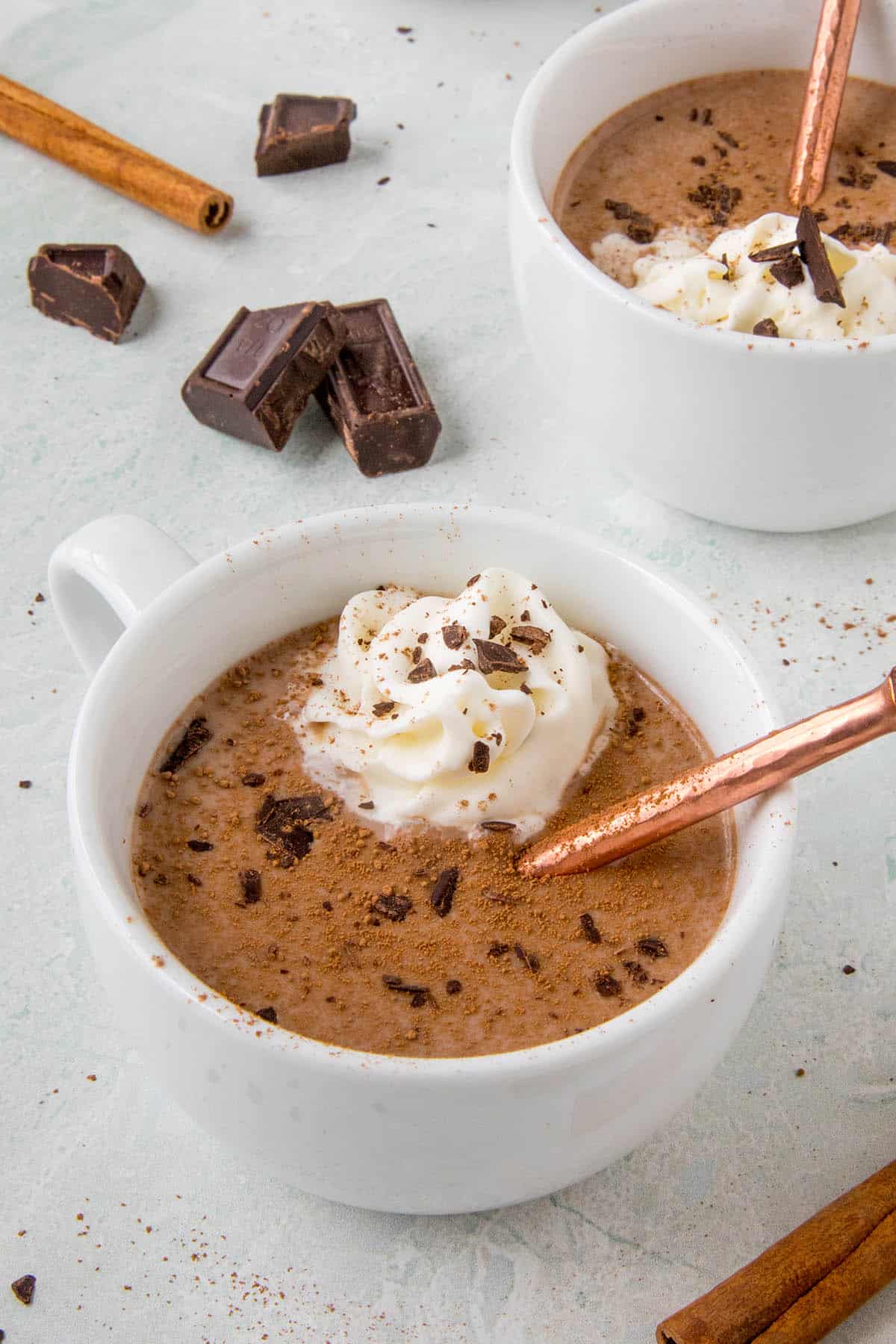Mexican hot chocolate in two white mugs with whipped cream and shaved chocolate on top.