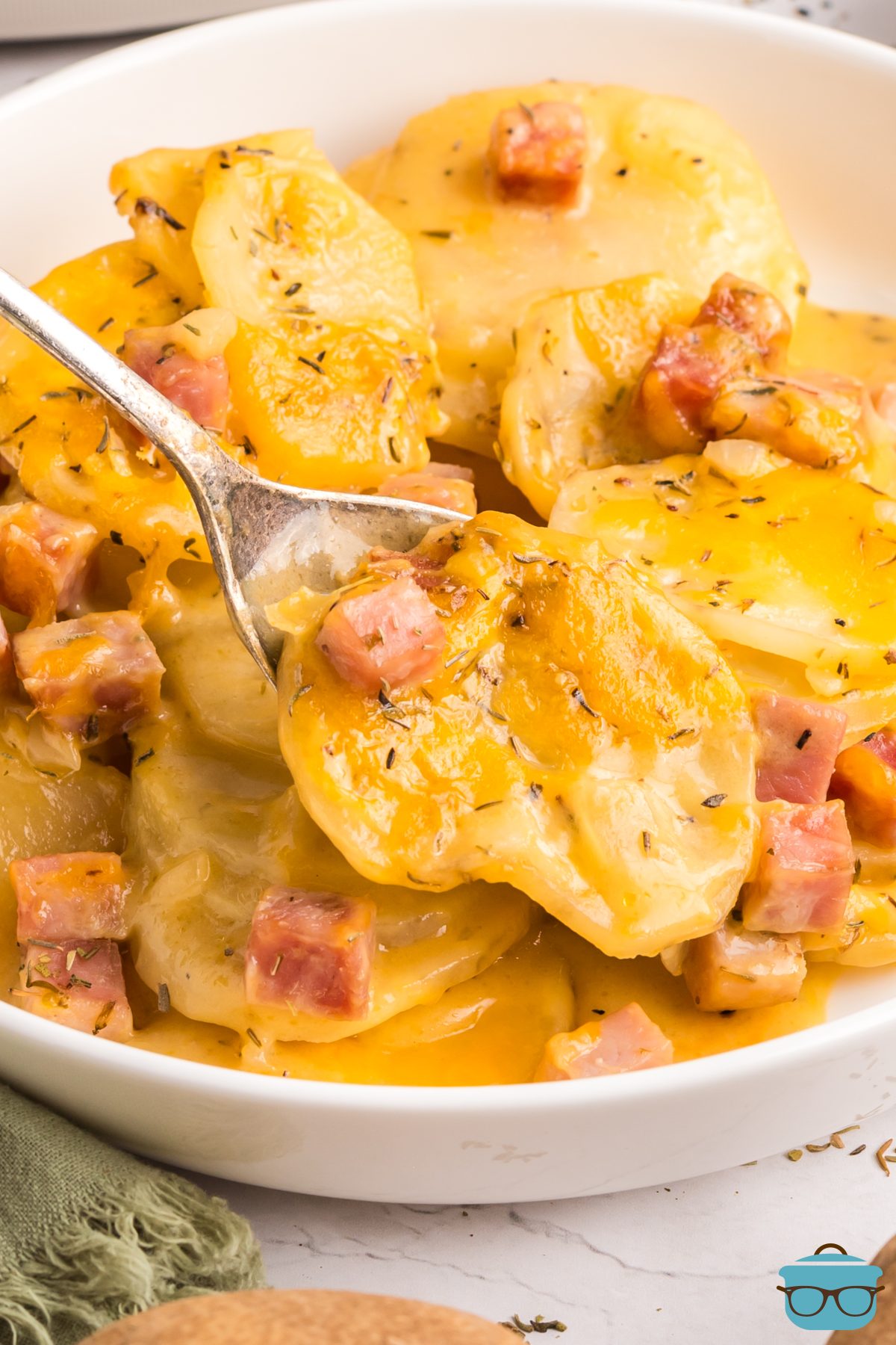 Crockpot ham and potatoes in a white bowl and lifted from the bowl on a metal spoon.