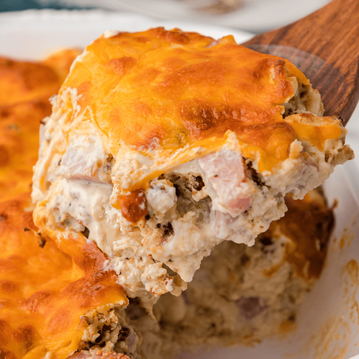 Cheesy cauliflower and ham casserole lifted from a casserole dish on a wooden spatula.