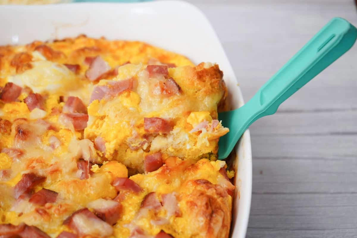 Ham and Swiss breakfast bake in a white casserole dish with a teal serving spoon.