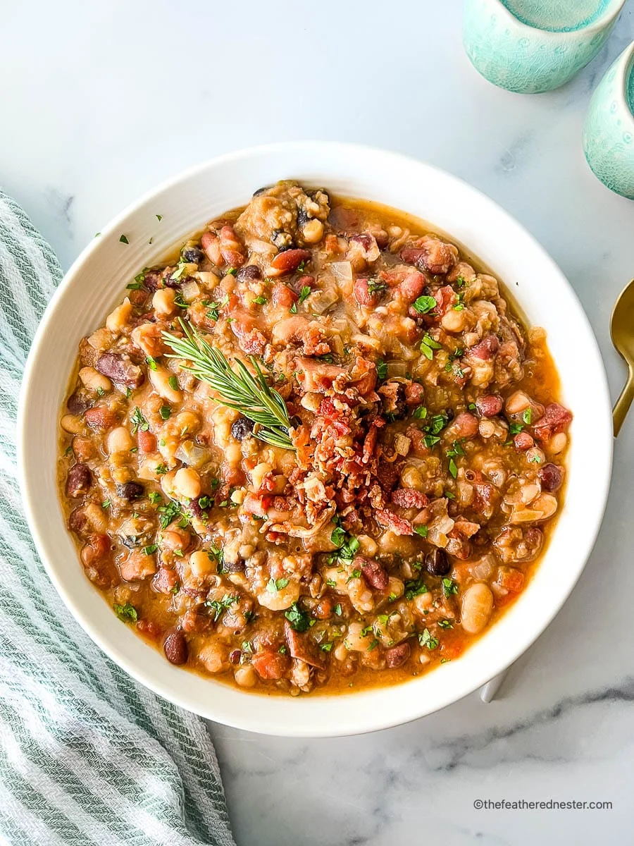 15 bean soup with ham in a white bowl with green garnish.
