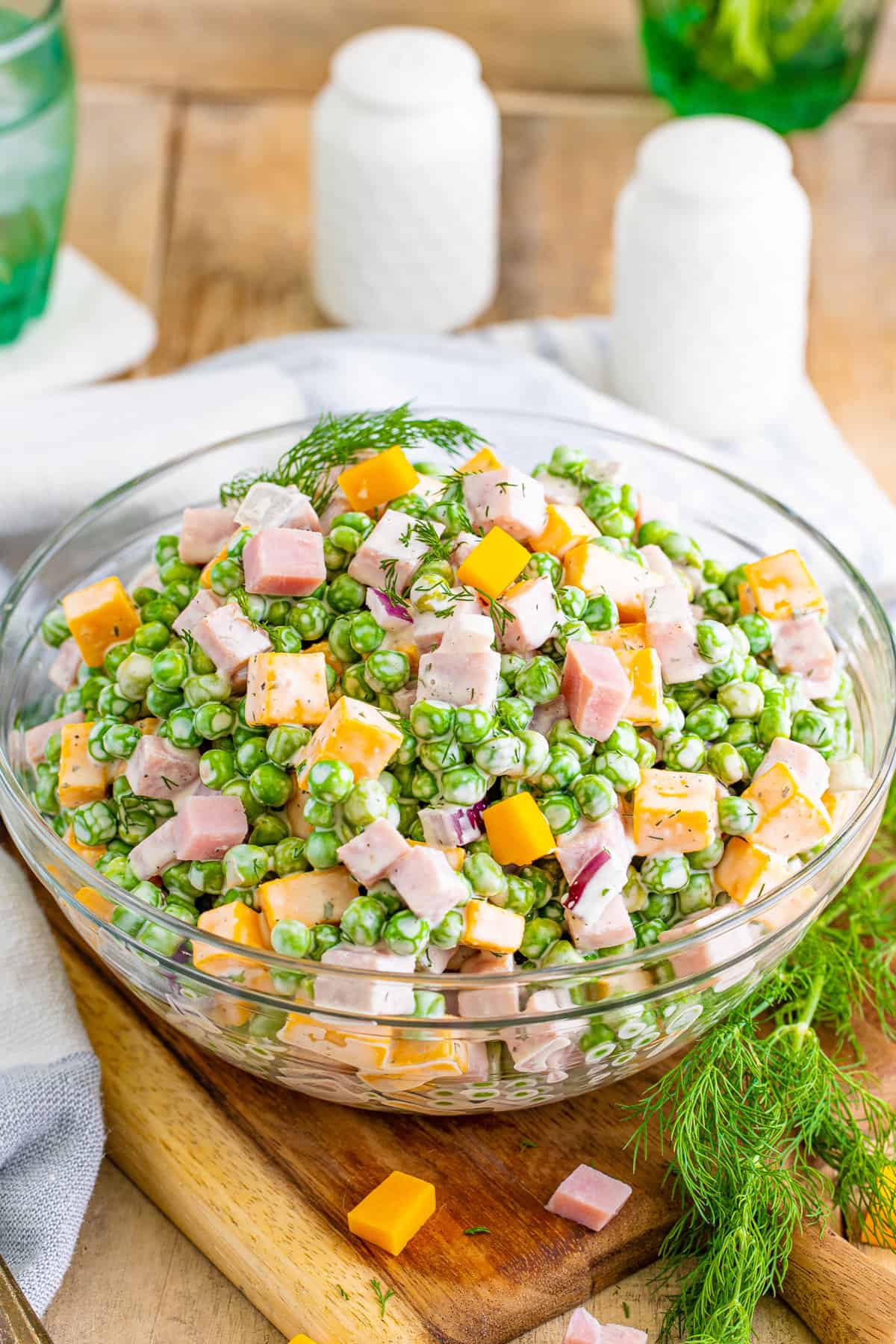 Pea salad with ham and cheese in a clear glass serving bowl.