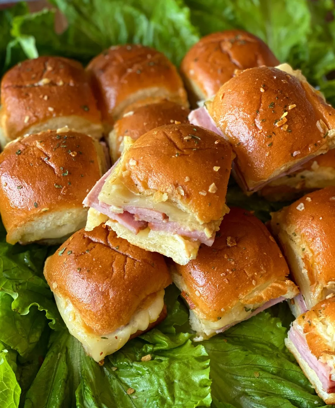 A stack of ham and cheese sliders on a bed of lettuce.