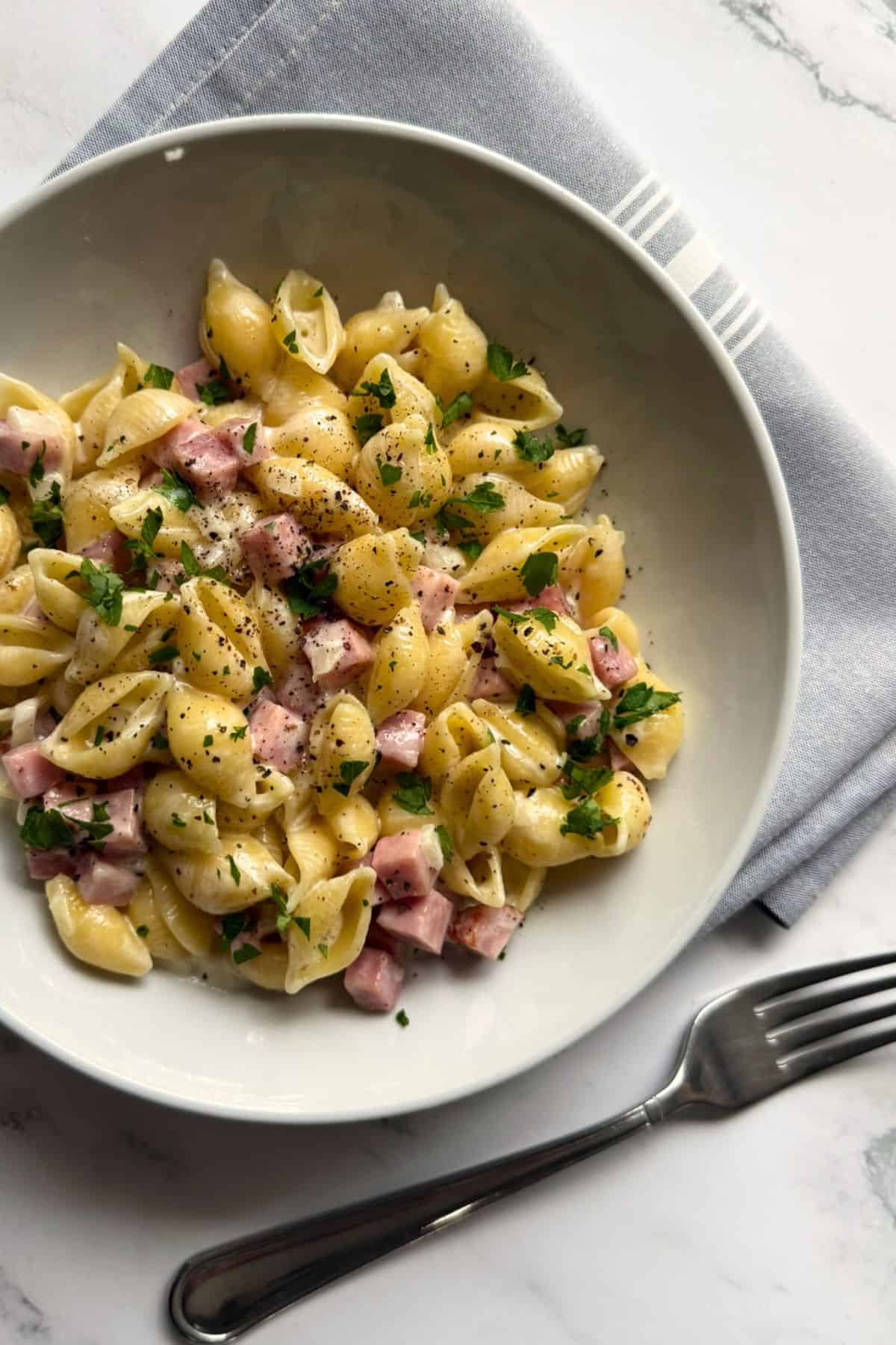 Pasta shells with ham and green garnish on a white plate.